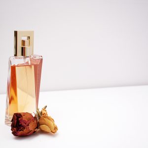 Elegant glass perfume bottle with luxurious design placed next to dried flowers against a minimalistic white background.