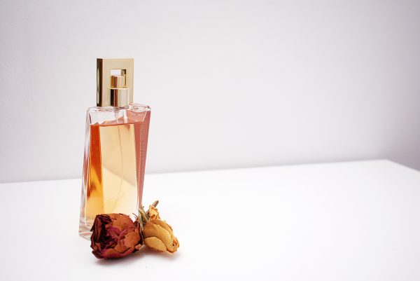 Elegant glass perfume bottle with luxurious design placed next to dried flowers against a minimalistic white background.